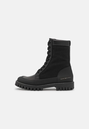 Black leather and fabric lace-up combat boot with thick tread sole and "Tommy Hilfiger" logo on heel.
