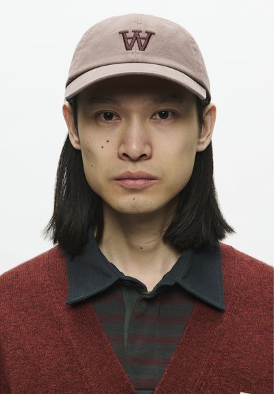 Casquette de baseball brun clair avec logo "W", cardigan bordeaux, chemise à col marine superposée et t-shirt rayé vert, tissu lisse, arrière-plan neutre.