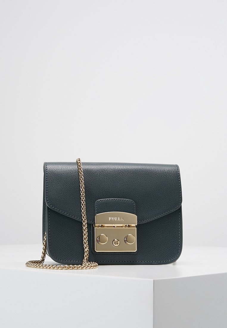 Liten mörkblå läderhandväska med strukturerad yta, gulddetaljer, kedjerem och framstängning med logotyp och dekorativa accenter.