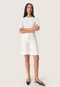 White ribbed short-sleeve top paired with high-waisted, knee-length white denim shorts. Black patent pointed-toe flats complete the outfit.
