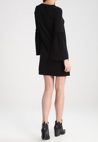 Black, long-sleeve dress with bell sleeves, fitted bodice, and a straight skirt. Worn with chunky black heeled ankle boots.