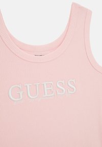 Rožinė briaunota marškinėlių su apvaliu iškirpimu ir balta siuvinėta "GUESS" logotipu. Audinys atrodo minkštas su tekstūruotu paviršiumi.