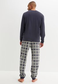 Maglietta a maniche lunghe blu navy abbinata a pantaloni da pigiama grigi con un design a griglia. I pantaloni hanno polsini elasticizzati e una vestibilità comoda.