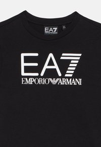 Camiseta de algodón negra con un gran logo blanco de EA7 Emporio Armani. Tiene cuello redondo y mangas cortas. Textura suave, diseño sencillo.