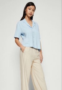 Svetlo modra srajca s kratkimi rokavi in ovratnikom, s gumbi spredaj, združena z bež širokimi hlačami. Gladek material z udobnim in sproščenim krojem.