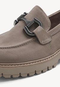Mocassin en suede taupe avec détail en métal noir en forme de mors et épaisse semelle en caoutchouc texturé.