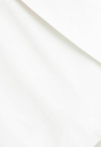 Vita sängkläder och kuddfodral prydligt arrangerade på en säng med mjukt naturligt ljus som kastar skuggor.