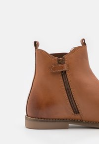 Bottines en cuir marron avec zip latéral, détails de couture, languettes au talon et à l'avant, et une semelle en caoutchouc plate.