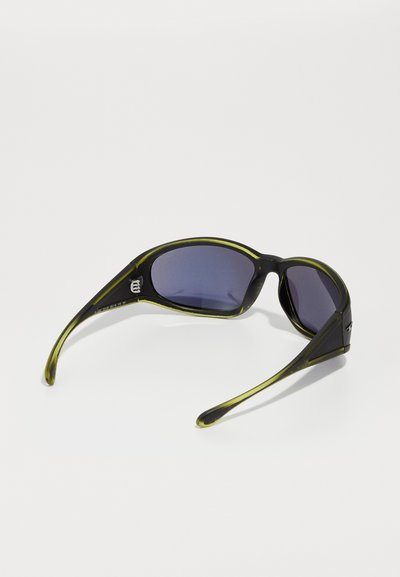 Lunettes de soleil noires avec un accent vert sur la monture, verres ovales et branches courbées. Les verres sont teintés foncés.