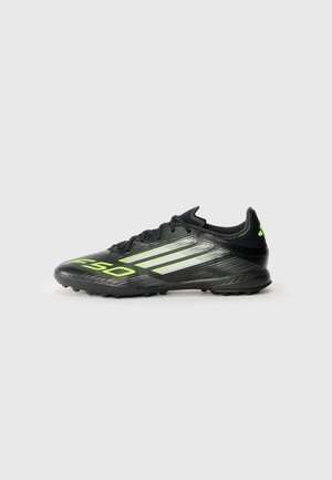 Black soccer shoe with a textured surface, featuring bright green accents and three white stripes. Designed for turf with a rubber outsole.