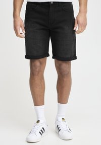 Shorts en denim noir avec un ourlet retroussé, cinq poches et une fermeture à bouton, associés à des chaussettes blanches et des baskets à rayures noires.