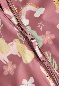 Tissu rose clair avec des motifs colorés de licornes, arcs-en-ciel et fleurs, avec une fermeture éclair visible assortie en rose.