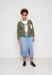 Olivengrønn strikket cardigan med rutenettmønster, hvit topp og jeans midi-skjørt med slisse foran. Sorte sneakers fullfører antrekket.