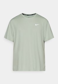 Světle zelené tričko s krátkými rukávy vyrobené z měkké tkaniny. Má bílé logo Nike na levé straně hrudi a černý branding na výstřihu.