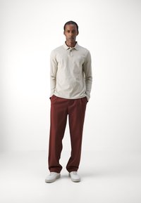 Beige langærmet polo-skjorte med et lille logo, parret med løse bordeaux bukser og hvide sneakers. Enkel og moderne design.
