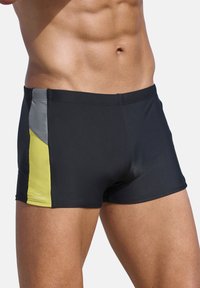 Schwarze Badeshorts mit einer figurschmeichelnden Passform und seitlichen Besätzen in Gelb und Grau. Hergestellt aus glattem, dehnbarem Material für Komfort und Bewegungsfreiheit.
