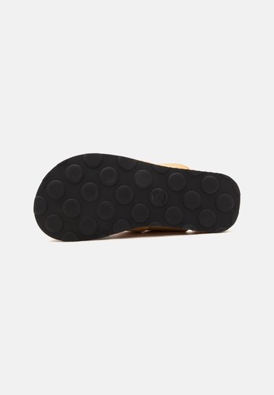 Semelle en caoutchouc noire d’une chaussure avec des motifs de bande de roulement ronds en relief sur un fond clair uni.