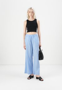 Zwarte cropped tanktop, blauw-witte gestreepte wijde broek, chunky zwarte hakken sandalen en een zwarte getextureerde handtas.