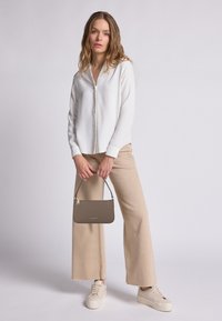 Camicia bianca con bottoni, pantaloni beige a gamba larga, sneakers color crema. Borsa marrone con texture e una piccola tracolla. Design semplice, palette di colori neutri.