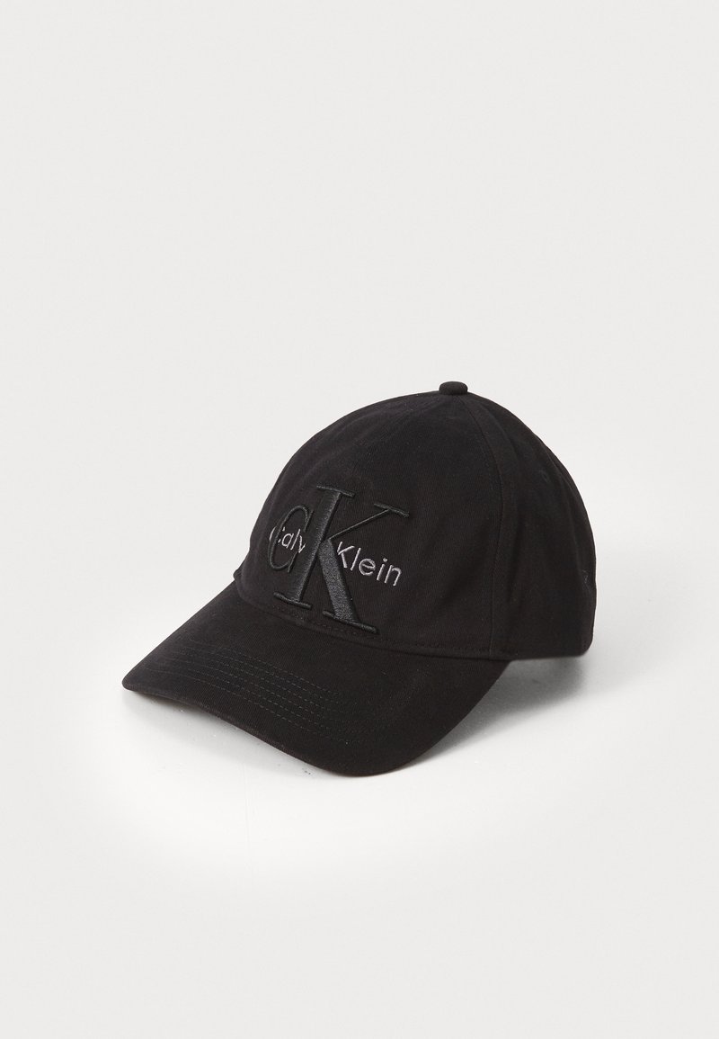 Mustaga puuvillast beise müts, millel on kaardus ääre, kus on tikitud "CK" logo ja "Calvin Klein" tekst stiilses disainis.