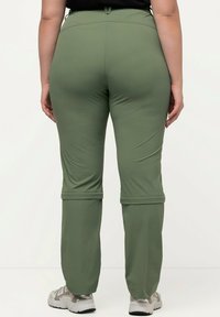 Pantaloni verdi, leggeri e elasticizzati con una vita regolabile e polsini arrotolati, abbinati a scarpe da ginnastica dai toni neutri.