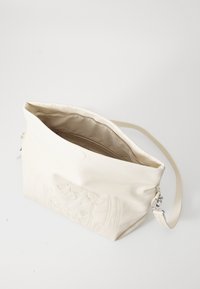 Borsa a spalla in pelle crema con un design floreale impresso, chiusura con zip e tracolla regolabile. Interno foderato in tessuto.