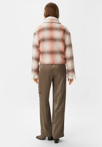 Puchowa kurtka w kratę w kolorach pomarańczowym, brązowym i kremowym; posiada wygodny kołnierz i ryflowane mankiety. Noszona z brązowymi satynowymi spodniami.