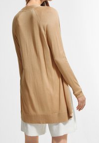 Ljusbeige långärmad cardigan med mjuk textur, sidoklyftor och ribbade ärmslut, med rund halsringning och avspänd passform.