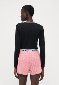 Black long-sleeve top with ribbed texture paired with pink shorts featuring a white geometric pattern and a branded elastic waistband.