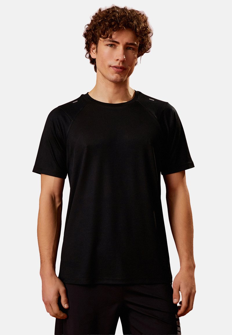 Sort crew-neck atletisk t-shirt, korte ærmer, ribbet tekstur, reflekterende accenter på skuldrene, tætsiddende design.