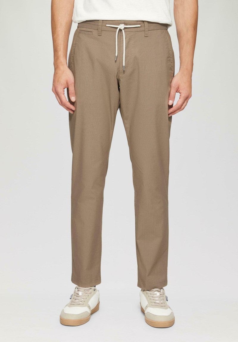 Beżowe, lekkie spodnie o prostym kroju z elastycznym paskiem w talii i kieszeniami z przodu. Połączone z białymi i beżowymi trampkami.