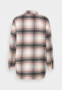 Chemise à manches longues à carreaux avec motif à carreaux noir, blanc et rose, montrée de dos sur fond blanc.