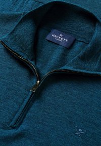 Turkusowa bluza rozpinana z prążkowanym kołnierzem, metalowym zamkiem błyskawicznym i wyszywanym logo na piersi. Wykonana z miękkiej dzianiny.