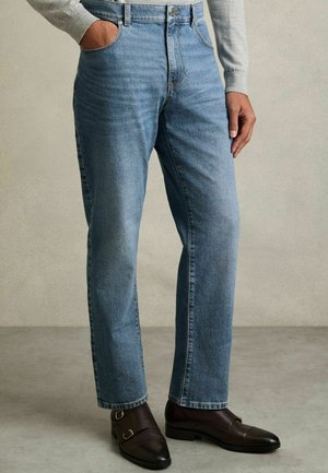 Jasnoniebieskie dżinsy z prostymi nogawkami, z zapięciem na zamek, pięcioma kieszeniami i lekkim przetarciem. W zestawie z ciemnobrązowymi butami.