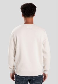 Light beige sweatshirt with long sleeves, round neckline, and ribbed cuffs. Features white text "WRONG FRIENDS" at the back neckline.