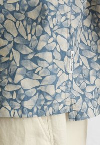 Lichte stoffen shirt met een blauw en crèmekleurig abstract patroon, met een klein merkje op de zijnaad. Korte mouwen, ontspannen pasvorm.