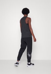 Canottiera nera senza maniche con una texture a macchie, abbinata a pantaloni neri larghi con dettagli stampati e polsini elasticizzati.