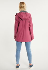Chaqueta de lluvia rosa resistente al agua con capucha, cordón ajustable y forro de felpa gris, combinada con jeans ajustados azules y zapatos navy.