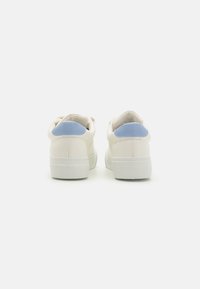 White leather sneakers with a smooth texture, light blue heel accents, and a flat rubber sole, featuring a minimalistic design.