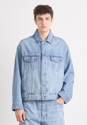 Light blue denim jacket with two chest pockets, silver buttons, and a casual cut. The fabric has a slightly faded texture.