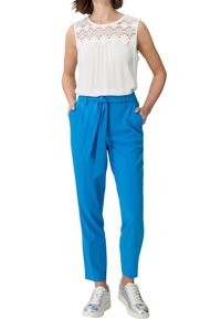 Top blanco sin mangas con detalles de encaje combinado con pantalones ajustados de color azul brillante y un cinturón, complementado con zapatillas plateadas.