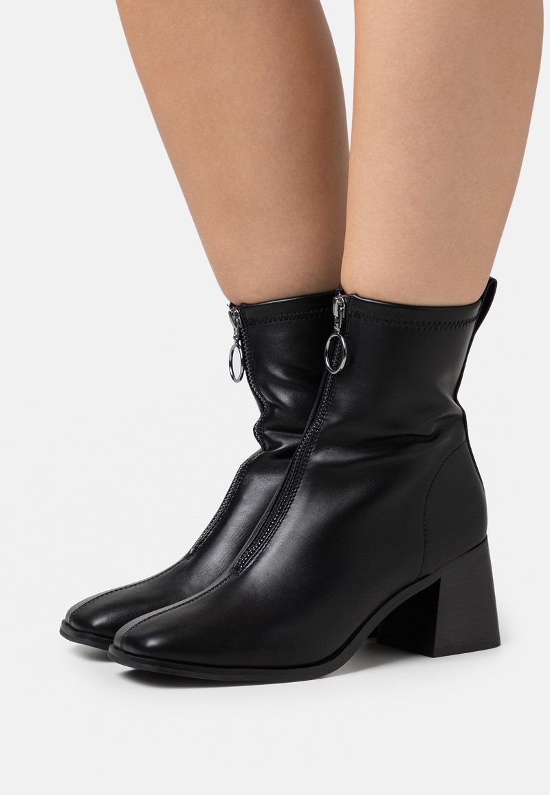 Bottines en cuir noir au design épuré, à bout pointu et à talon bloc de hauteur intermédiaire, dotées de doubles zips et de tirettes rondes.