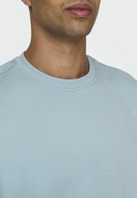 Helles blaues T-Shirt mit Rundhalsausschnitt aus weicher Baumwolle, das eine glatte Textur und ein einfaches, sauberes Design ohne sichtbare Logos oder Muster aufweist.