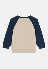 Beige og marineblå langermet genser med ribbestrikkede mansjetter og hem, vist på en hvit bakgrunn.
