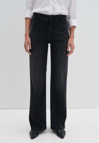 Mustat denimi leveälahkeiset housut korkealla vyötäröllä, viisi taskua ja samanvärinen ommel, yhdistettynä mustiin teräväkärkisiin kenkiin ja valkoiseen paitaan.