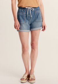 Shorts di jeans in azzurro chiaro, con cintura a cordino, due tasche anteriori e risvolti. Indossati con sandali a piattaforma metallici oro.