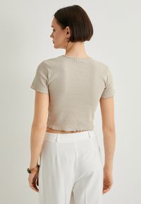 Camiseta corta de canalé beige claro con mangas cortas, con un dobladillo sin terminar. Combinada con pantalones blancos de tiro alto.
