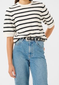 Pull en tricot rayé crème et noir, avec des manches courtes et un col rond. Associé à un jean bleu clair taille haute et une ceinture noire.