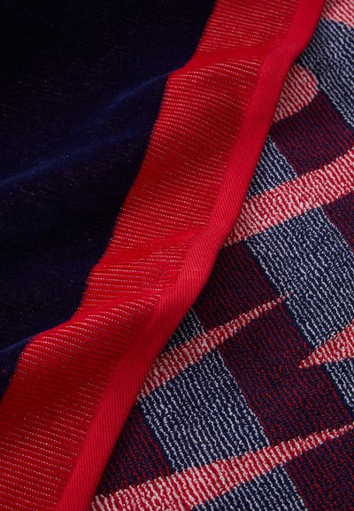 Tissu à carreaux bleu marine et rouge, avec une texture lisse et une bordure rouge proéminente le long du bord, agrémenté de détails complexes.
