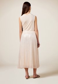 Top senza maniche di un tenue rosa pallido abbinato a una gonna midi plissettata e luccicante, accentuata da una morbida vita e una finitura strutturata. Sandali flat visibili.